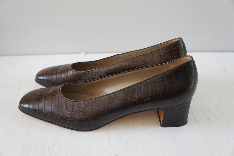 May include: A pair of brown leather heeled pumps with a crocodile embossed pattern.