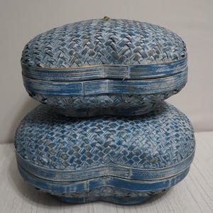 May include: Two blue woven heart-shaped baskets stacked on top of each other. The baskets are made of a woven material and have a distressed blue paint finish.