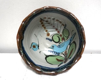 May include: Hand-painted ceramic bowl with a brown rim and a white interior. The bowl features a blue bird, green leaves, and a butterfly design. The rim has a dark blue accent.