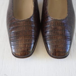 May include: A pair of brown leather flats with a crocodile-embossed pattern. The shoes have a pointed toe and a low heel.