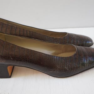 May include: A pair of brown leather pumps with a low block heel. The shoes have a textured, alligator-like pattern.