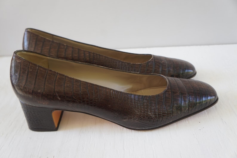 May include: A pair of brown leather pumps with a low block heel. The shoes have a textured, alligator-like pattern.