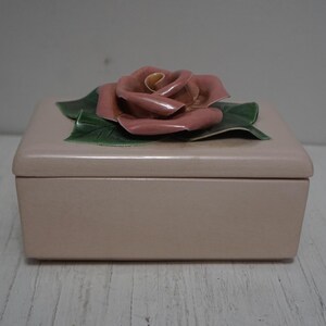 May include: A pale pink wooden box with a 3D pink rose on the lid. The rose has green leaves and a yellow center.