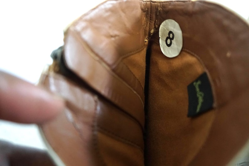 K&ouml;nnte beinhalten: Nahaufnahme des Innenraums eines braunen Lederstiefels mit einem Gr&ouml;&szlig;enetikett 8. Der Stiefel hat einen Rei&szlig;verschluss an der Seite und ein braunes Lederfutter.