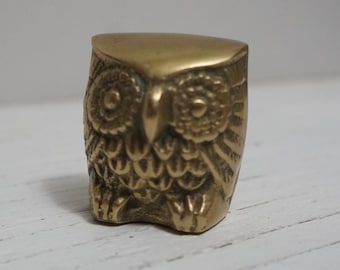 May include: A small, gold-colored brass owl figurine. The owl is sitting with its wings folded and has detailed features, including eyes, beak, and feathers.