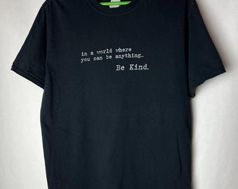 May include: Black t-shirt with white text that reads "in a world where you can be anything... Be Kind."