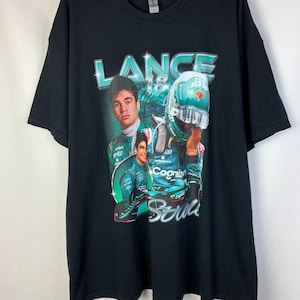 May include: Black t-shirt with a graphic print of a race car driver wearing a green helmet and a green racing suit. The text "LANCE 18" is printed above the image.