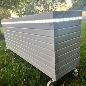 May include: A white wooden planter box with a built-in LED light strip. The planter is on wheels and has a slatted design.