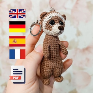 Op de afbeelding: Gehaakte amigurumi sleutelhanger met een bruine en witte otter met zwarte ogen. De sleutelhanger is bevestigd aan een zilveren sleutelring. De otter houdt een klein, bruin, gehaakt hart vast.