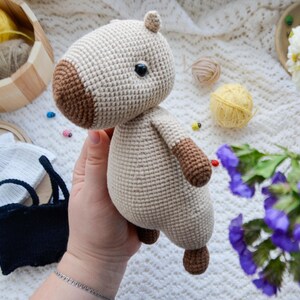 May include: A crocheted stuffed animal in the shape of a horse. The horse is beige with brown accents and has a black eye. The horse is being held in a person's hand.