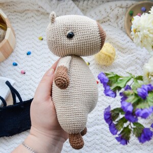 May include: A crocheted stuffed animal in the shape of a brown and white dog. The dog is being held in a person's hand. The dog has a brown nose and black eyes.