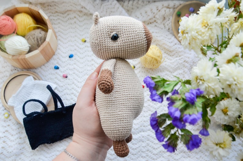 May include: A crocheted stuffed animal in the shape of a brown and white dog. The dog is being held in a person's hand. The dog has a brown nose and black eyes.