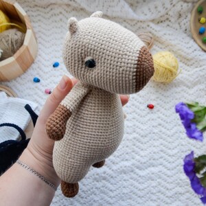 May include: A crocheted stuffed animal in the shape of a capybara. The capybara is beige with brown accents and has a black eye.