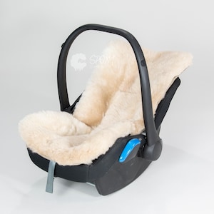 Può includere: Seggiolino auto nero per bambini con un inserto in pelle di pecora color crema e soffice. Il seggiolino ha una maniglia nera e dettagli blu e grigi. Il seggiolino è progettato per la sicurezza e il comfort.