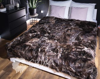 May include: A bed with a brown faux fur blanket. The bed has white pillows and a light pink pillow. The room has black walls and a black dresser. A framed picture hangs on the wall.