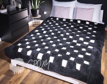 May include: A black and white checkered pattern blanket on a white bed frame. The blanket has a plush texture and covers the bed, with two white pillows and two pink pillows visible. The room has dark walls and a wooden floor.