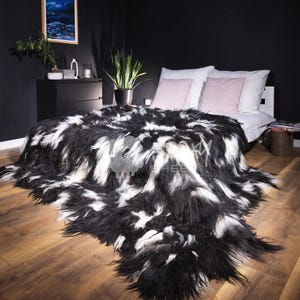 Pode incluir: Uma manta de pele sintética preta e branca sobre uma cama com roupa de cama branca e almofadas rosa. O quarto tem paredes escuras e piso de madeira. Uma imagem emoldurada está pendurada na parede.