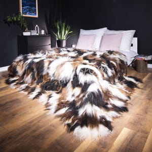 Könnte beinhalten: Eine luxuriöse Kunstfell-Decke in Braun-, Schwarz- und Weißtönen bedeckt ein Bett mit weißen Kissen und einem rosa Akzentkissen. Die Textur der Decke verleiht dem Schlafzimmer Wärme. Der Raum hat dunkle Wände und Holzböden.
