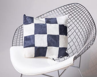 Puede incluir: Una silla moderna con asiento blanco y respaldo de alambre cromado. Un cojín decorativo con un patrón de tablero de ajedrez en azul marino y blanco descansa sobre la silla. El cojín está hecho de un material texturizado.