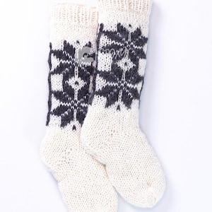 May include: A pair of off-white knit socks with a snowflake pattern in dark gray. The socks have a ribbed cuff and are made of a thick, warm material, perfect for cold weather. The snowflake design adds a touch of winter charm.