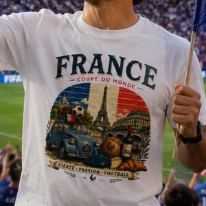 May include: A white t-shirt featuring a graphic print with the text FRANCE, COUPE DU MONDE, FIERTE, PASSION, FOOTBALL, depicting the Eiffel Tower, a blue vintage car, a soccer ball, a bottle of wine, and a croissant against a French flag background.