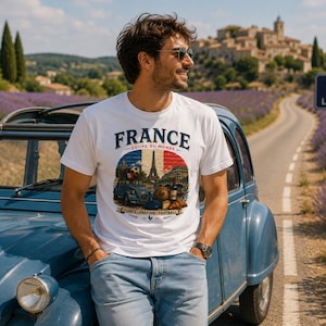 May include: A white short-sleeve t-shirt featuring a graphic print with the text FRANCE COUPE DU MONDE FIERTE PASSION FOOTBALL. The design includes a blue car, the Eiffel Tower, a soccer ball, a bottle of wine, and a croissant over a flag.