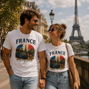 May include: Two white t-shirts featuring a graphic print with the text FRANCE COUPE DU MONDE, FIERTE PASSION FOOTBALL. The design includes a blue car, a soccer ball, a croissant, a wine bottle, and the Eiffel Tower against a French flag background.