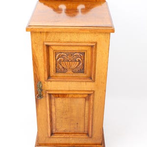 May include: A light brown wooden cabinet with a carved floral design on the door and a decorative top. The cabinet has a small brass handle and is likely used for storage. The measurements are in centimetres.