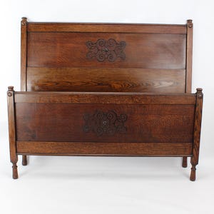 May include: A dark brown wooden bed frame with a headboard and footboard. The headboard and footboard feature decorative carved floral designs. The bed frame has four legs and is made of solid wood.