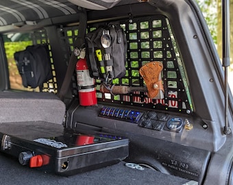 May include: Interior view of a vehicle's back area, featuring a black storage case, a red fire extinguisher, and a black organizer with various tools. A brown leather axe sheath is also visible.