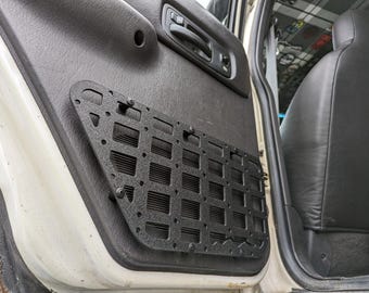 Puede incluir: Panel organizador de carga de metal negro para una puerta de vehículo. El panel tiene un patrón de cuadrícula con múltiples puntos de fijación.