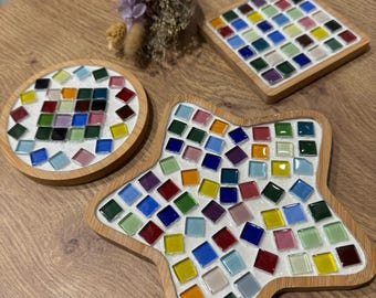 Pode incluir: Três  tapetes de mosaico coloridos com fundo branco e moldura de madeira. Os tapetes são em forma de círculo, estrela e quadrado.