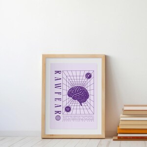 May include: A framed art print featuring a purple brain illustration within a geometric grid. The word "RAWFEAR" is printed vertically on the left side. Additional text and starburst graphics are also present. The frame is made of light-colored wood.