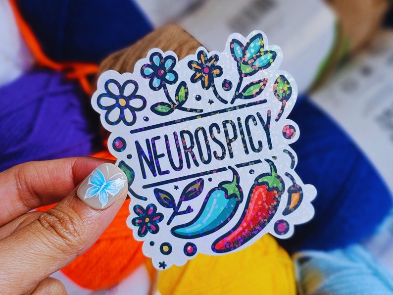 May include: White sticker with a colorful floral design and the text "Neurospicy". The sticker features a red and green chili pepper, a blue and green chili pepper, and a yellow chili pepper.