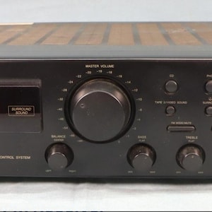 以下が含まれることがあります： 黒色のJVC RX-318 FM/AMレシーバー。複数のボタン、ノブ、デジタルディスプレイを備えています。レシーバーにはマスターボリュームノブとさまざまな入出力オプションがあります。「Surround Sound」の文字が前面パネルに表示されています。