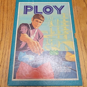 May include: Vintage board game box titled "PLOY." The box features a man in a purple turtleneck reaching toward game pieces. The background shows a futuristic cityscape. The text reads "Strategic Game of Maneuver and Capture."