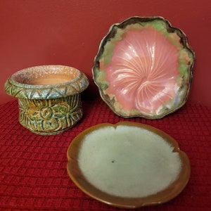 Pode incluir: Três pratos de cerâmica em verde, marrom e rosa com desenhos florais. Os pratos estão sobre um fundo vermelho.