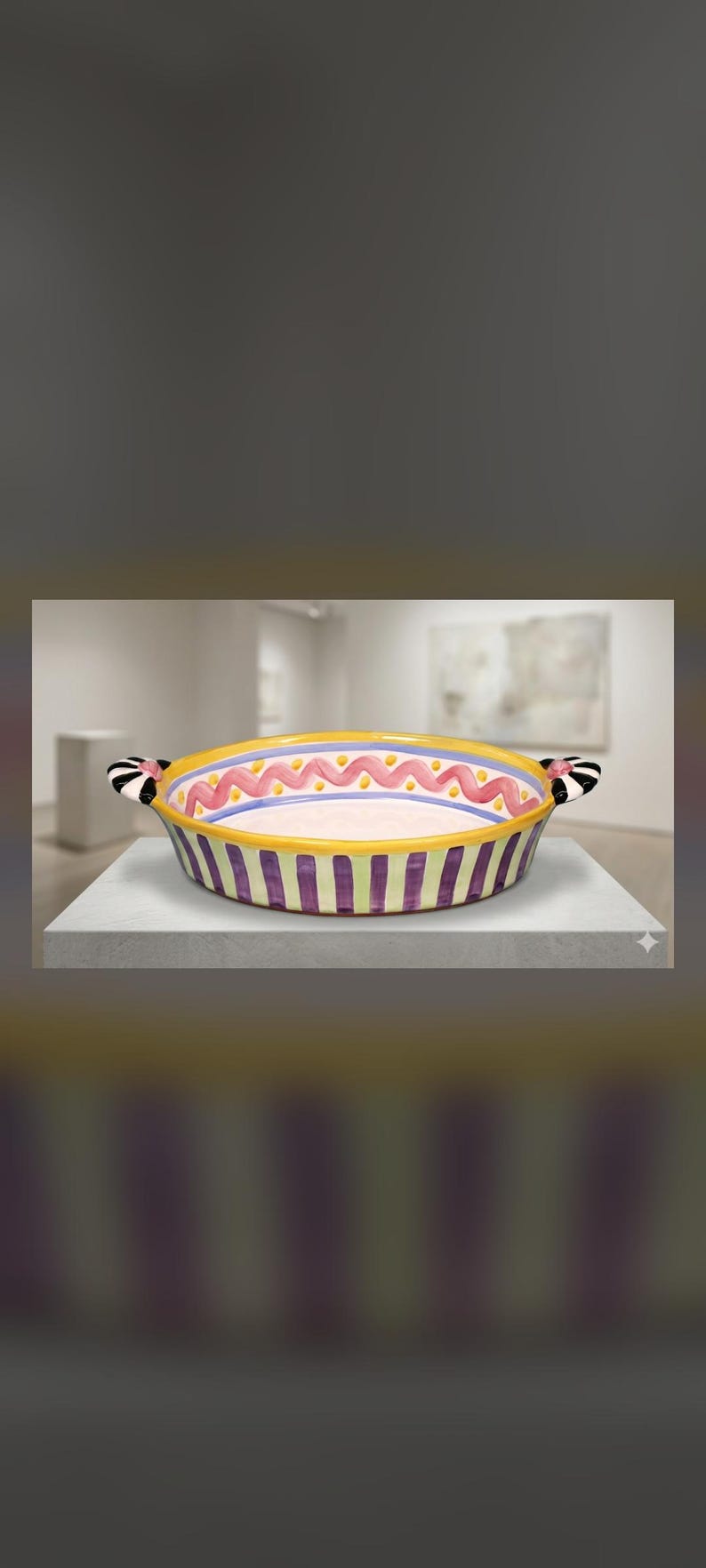 May include: A round ceramic baking dish featuring a yellow rim, a pink wavy line pattern, and a purple and yellow striped exterior. The dish includes two side handles decorated with black and white stripes and small pink accents.