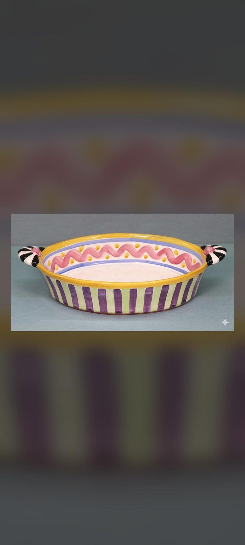 May include: A round ceramic baking dish with two side handles. The exterior features vertical purple and light green stripes. The interior rim is decorated with a yellow border, a blue line, and a pink wavy line with small yellow dots.