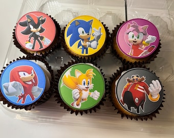 May include: Six cupcakes decorated with images of Sonic the Hedgehog characters. The cupcakes are in a clear plastic container. The characters are Sonic, Tails, Knuckles, Shadow, Amy Rose, and Dr. Eggman.