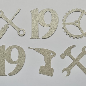 May include: Silver glitter paper cutouts of the number 19, a wrench and screwdriver, a drill, a gear, and a hammer and wrench. The number 19 is repeated twice.