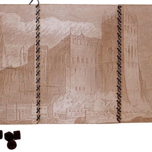 Op de afbeelding: Een vintage lederen gebonden dagboek met een gedetailleerde illustratie van een stadsbeeld. Het dagboek is gesloten en heeft een bruine lederen omslag met een gestikte binding.