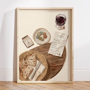 May include: A framed art print depicting a wooden table with a basket of sliced bread, a silver knife, a small plate of coins, a matchbox with an Eiffel Tower illustration, a glass of red wine, and a cafe receipt labeled Cafe du Coin.