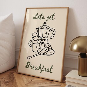 Może przedstawiać: Beżowy plakat z czarnymi rysunkami kawiarki, kubka, łyżki i ciast. Tekst "Lets get Breakfast" jest napisany zielonym kursywą.