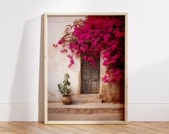 May include: A wooden framed print of a weathered door with a vibrant pink bougainvillea vine growing over it. The door is closed and has a rustic, aged look. The bougainvillea flowers are in full bloom and create a beautiful contrast against the white wall.