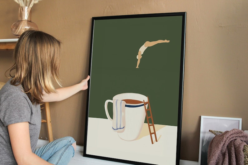 May include: A framed illustration of a person diving into a large coffee mug. The mug has a white background with a blue stripe and a brown liquid inside. A white towel hangs on the side of the mug and a wooden ladder is next to it. The background is a dark green color.