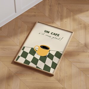 May include: A framed print with a yellow coffee cup on a black and white chequered background. The text reads "Un Caf&eacute; s'il vous pla&icirc;t!"