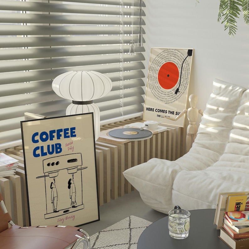 May include: A white couch with a white throw pillow. A wooden table with a record player and a black record on it. A black framed poster with the text 'COFFEE CLUB' and a coffee maker illustration. A white framed poster with the text 'HERE COMES THE SUN' and a red circle with a black line through it. A white lamp with a white shade. A brown leather chair with a white rug underneath.