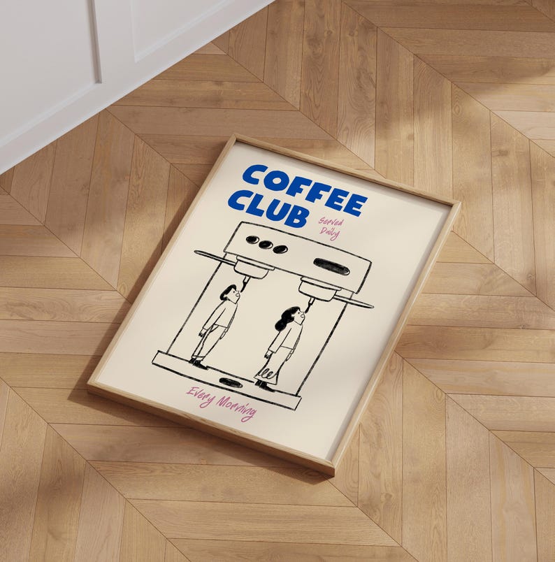 May include: A framed poster with a white background and black illustrations. The poster says 'COFFEE CLUB' in blue text with the words 'served daily' in smaller blue text. The poster shows two people drinking coffee from a coffee machine. The poster says 'Every Morning' in pink text.