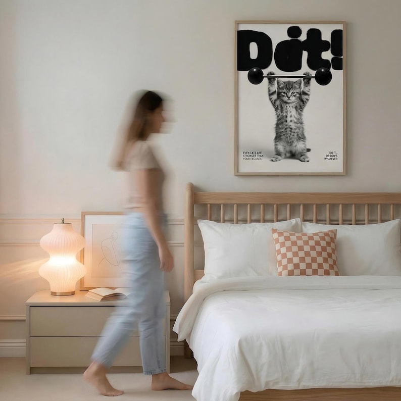 May include: A bedroom scene featuring a wooden bed with white bedding and a checkered pillow. A framed poster with the word "Do it!" and a cat lifting weights hangs above the bed. A woman walks past the bed.
